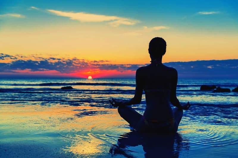 Person meditating on a shoreline at sunset